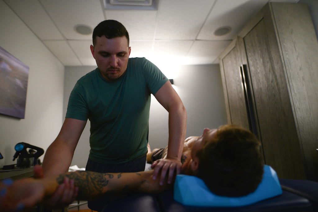 Chris supports Carter’s forearm and upper arm while Carter rests on the treatment table.